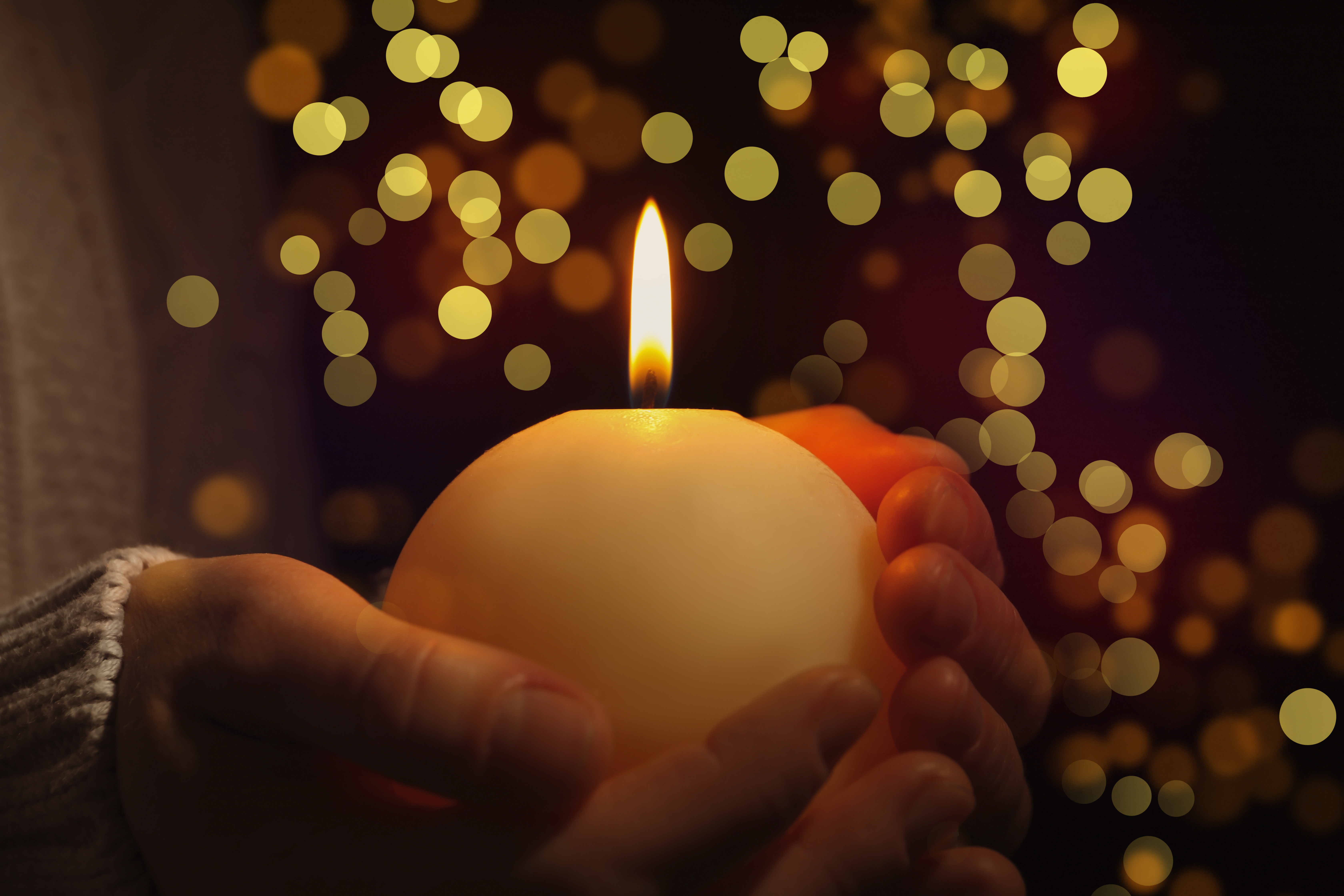 Closeup view of woman holding burning candle in darkness, bokeh effect. Christmas Eve stock phot
